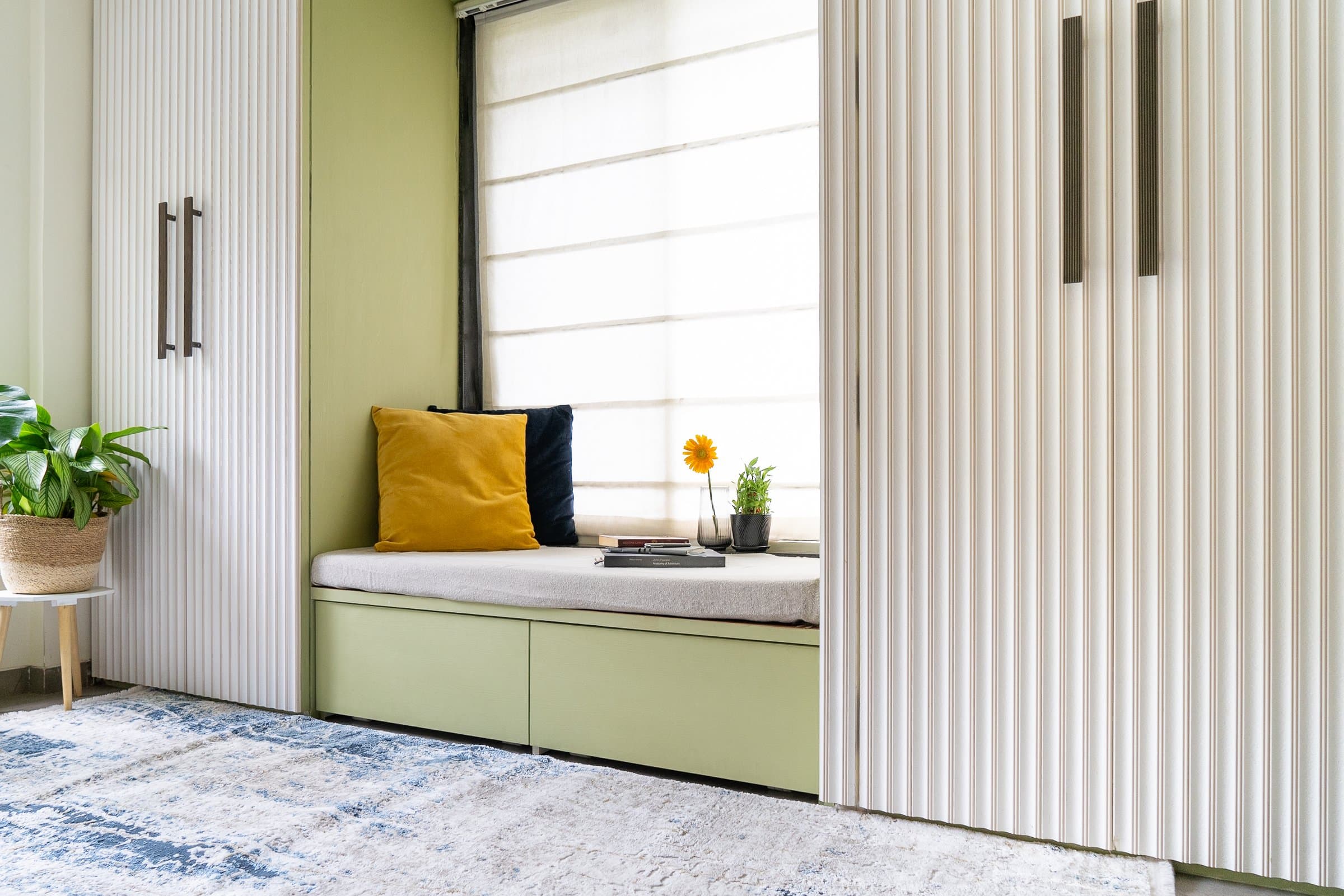 Sage green window seat with fluted white and green wardrobe doors, mustard and navy cushions, blue and white patterned rug