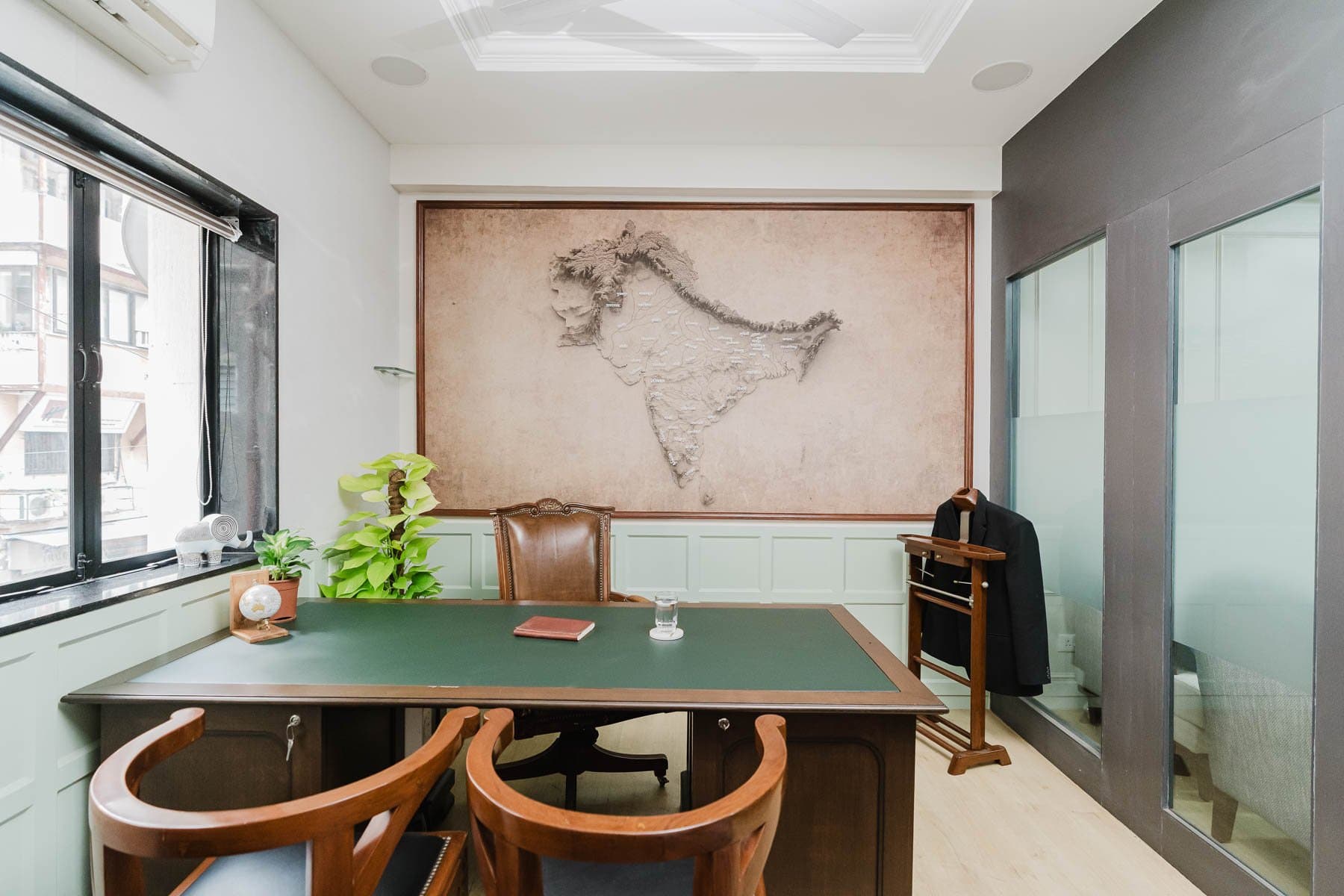 Cream panelled wall with a framed Gateway of India print, teardrop wall sconces, a white sofa with chevron cushions and a tufted leather ottoman